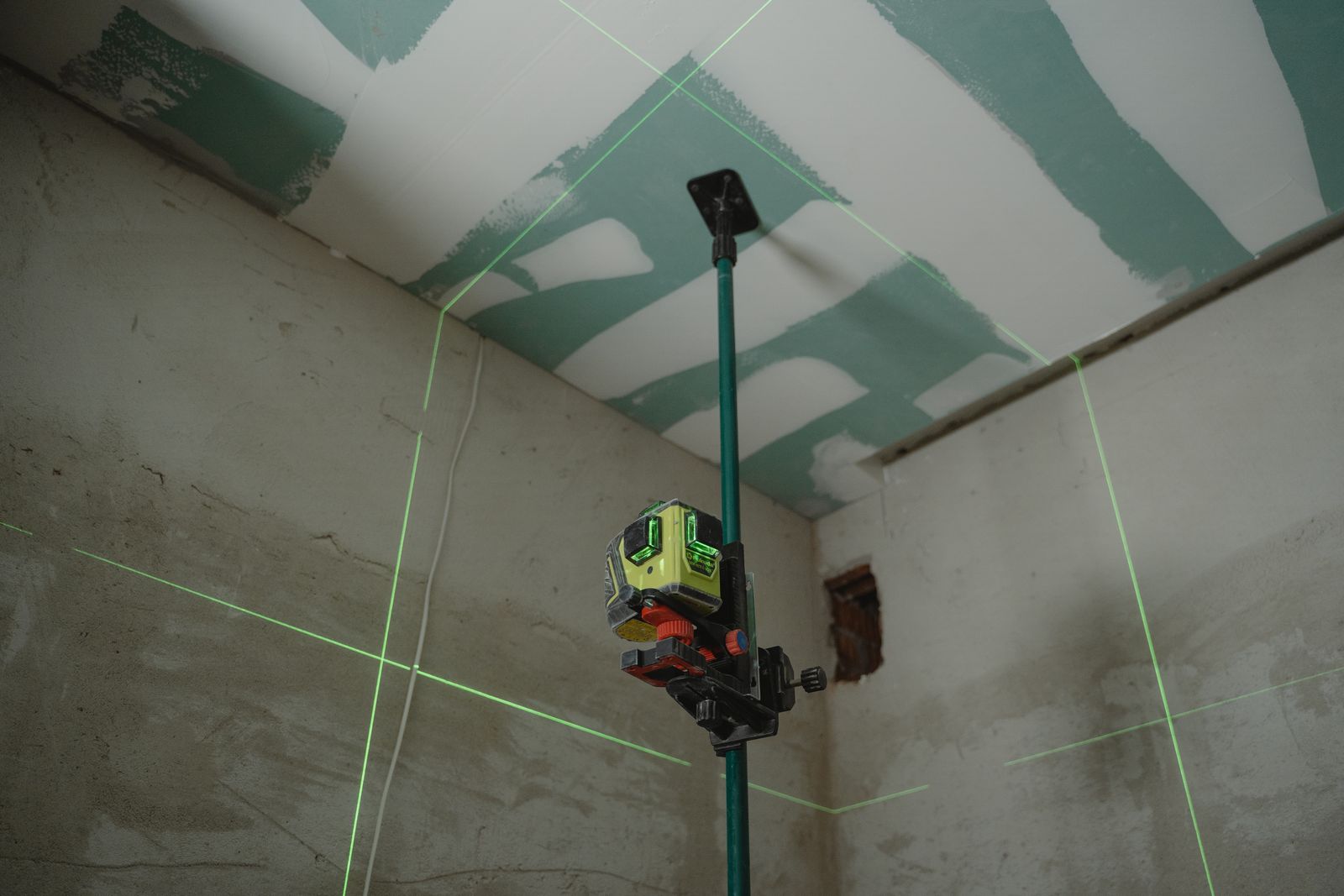 A green laser level projecting lines across an unfinished room